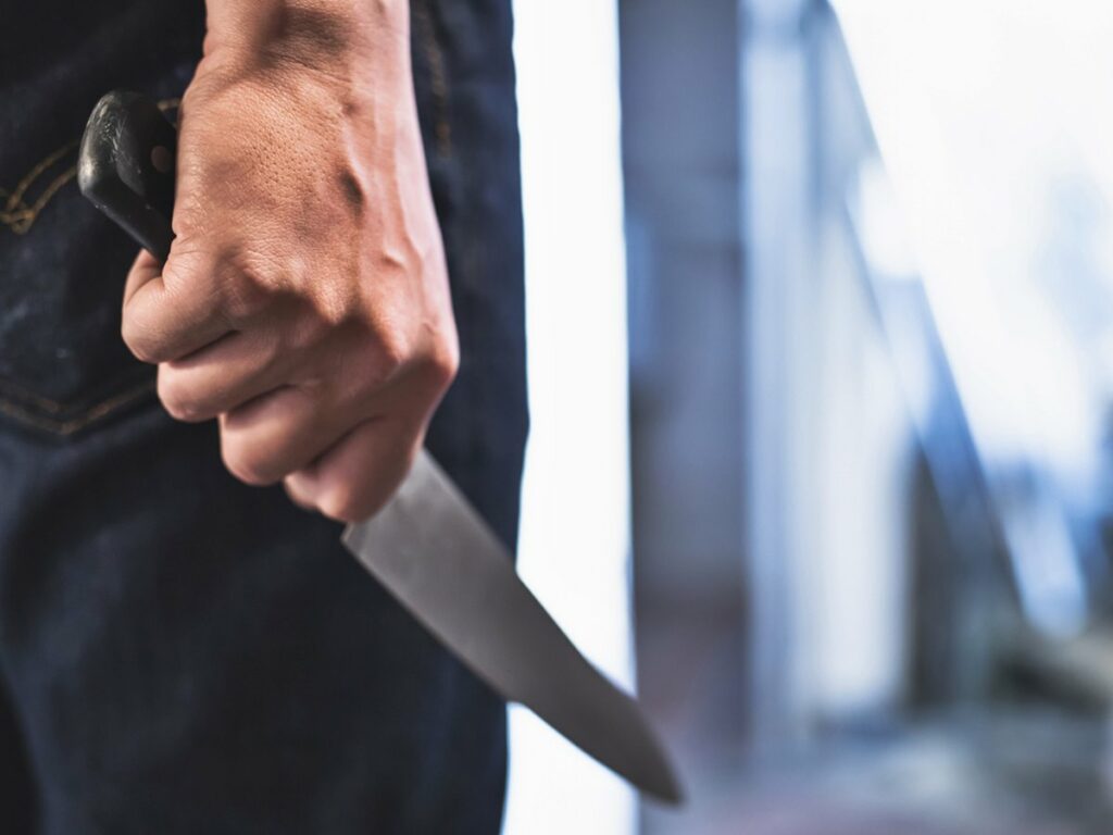 image of a robbers hands holding a knife in the shadows.