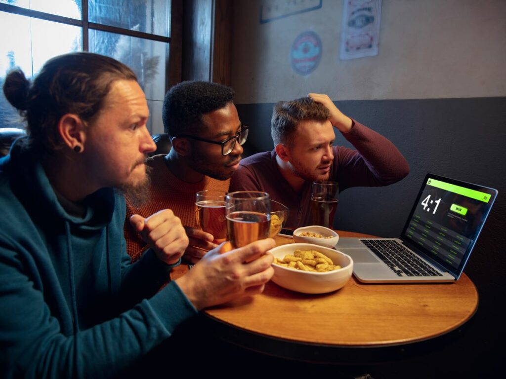 Device screen with application for betting and score. Device with match results on screen, excited fans on background during match. Gambling, betting, sport, finance, modern technologies concept.