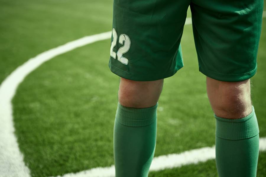 The legs of soccer football player training football on green grass field