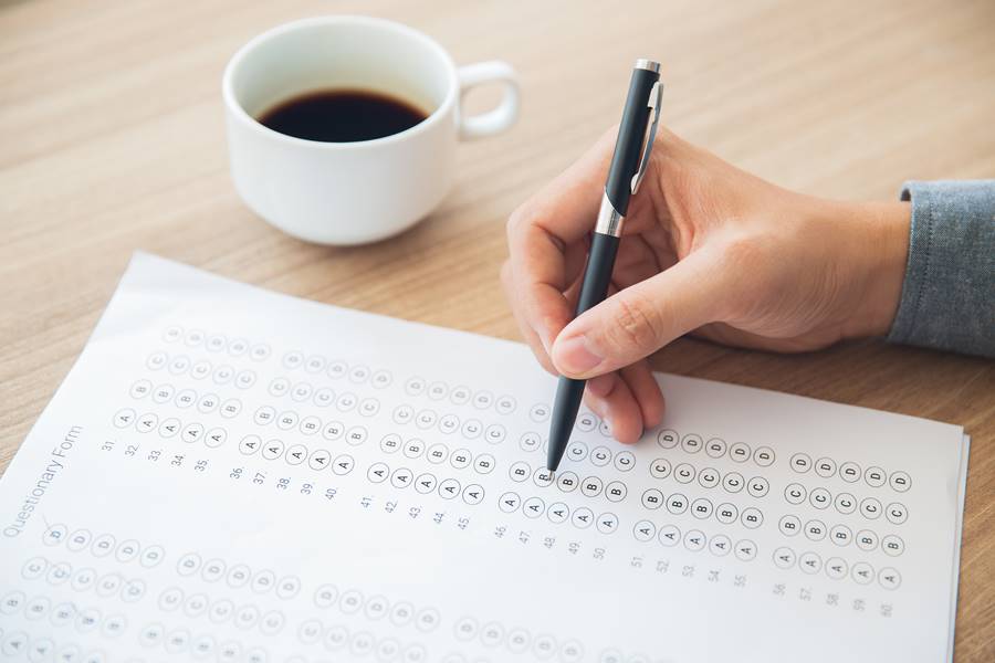 Hand of man holding ballpoint pen and answering questionary form. Male student sitting at table and writing test