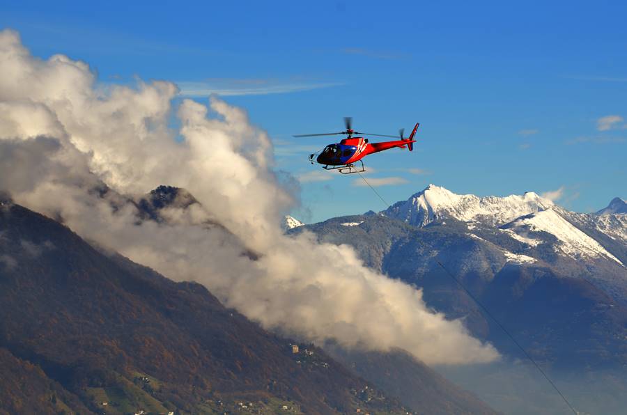 A helicopter flying among the clouds above the snow-capped mountains