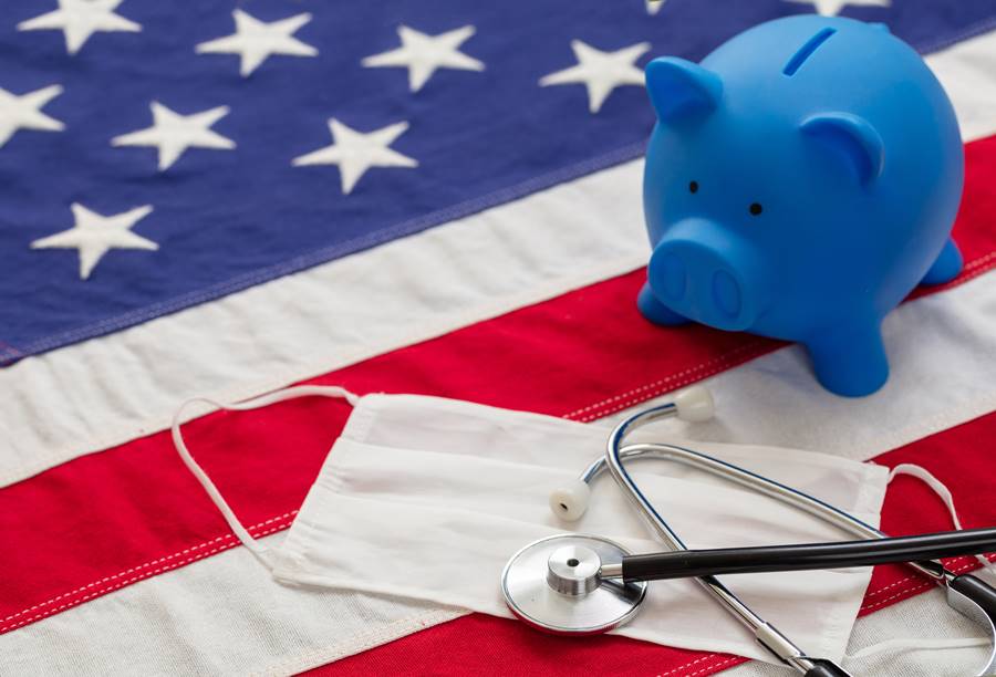 USA health care cost, coronavirus days. Medical stethoscope, protective face mask and piggy bank on a US of America flag, banner.