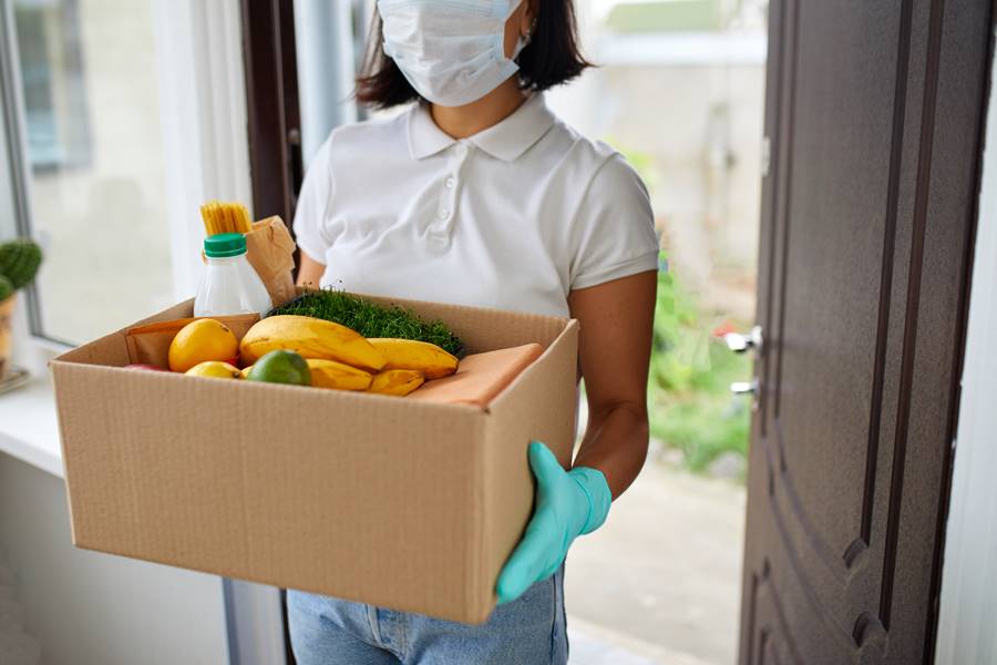 Volunteer woman in white protective mask and gloves delivery donation box at home, Courier with packing box with food, contactless delivery, Service quarantine pandemic coronavirus.