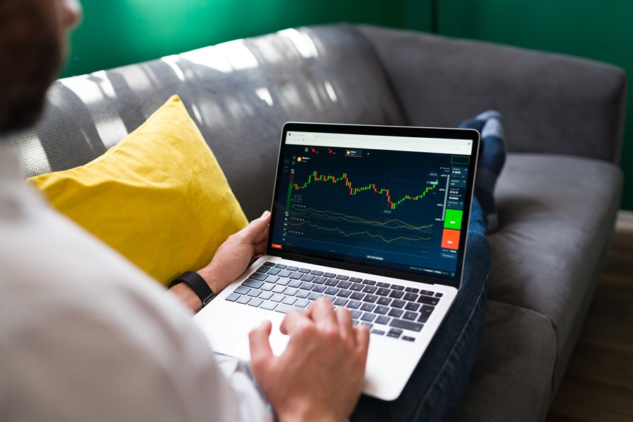 Trading finances. Young man resting on the couch while checking the stock market on the laptop