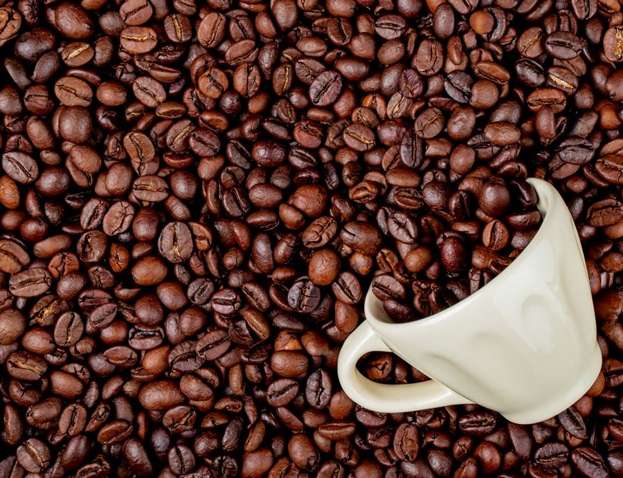 top view of roasted coffee beans scattered from a ceramic cup on coffee beans background