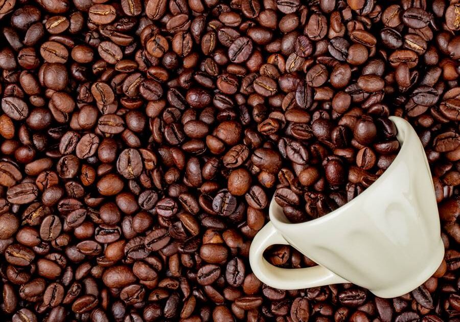 top view of roasted coffee beans scattered from a ceramic cup on coffee beans background