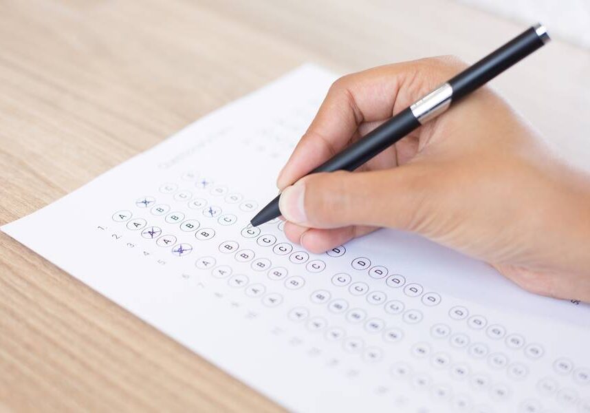 Closeup of hand holding pen and filling out questionary form on table